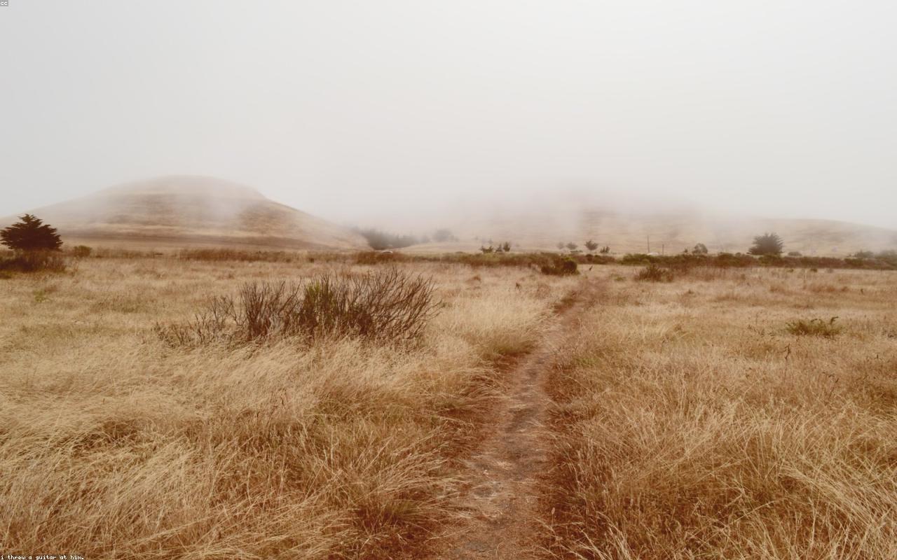 A person standing on a mountain path above mist and distant terrain